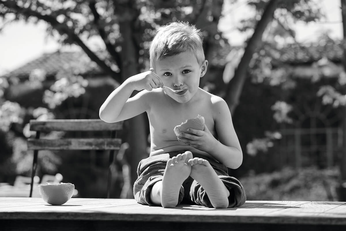 Small boy eating yoghurt pot in a scene of natural beauty