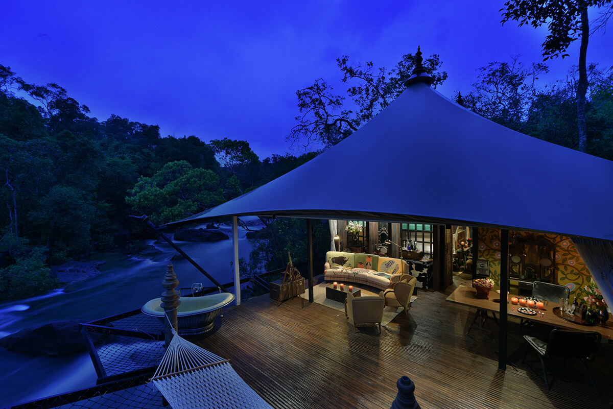 Luxury safari tent at night with wooden deck and outdoor bath tub in Cambodian forest