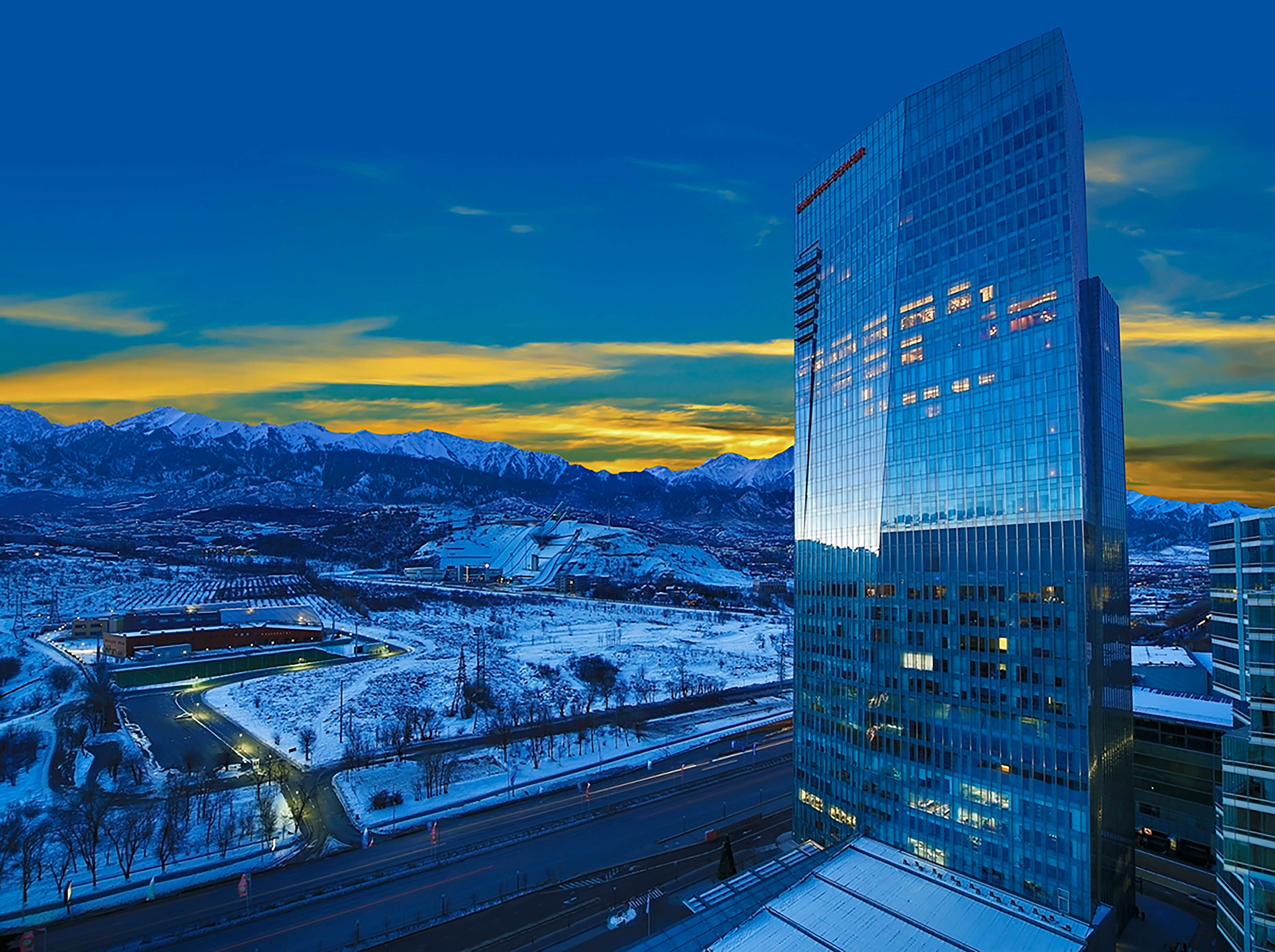 Luxury hotel Ritz Carlton Almaty against sunset and snow backdrop