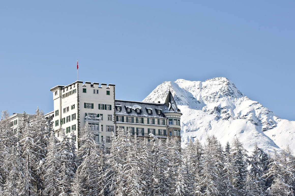 Waldhaus Sils five star swiss hotel rising up from the trees in front of the snowy mountains in Winter
