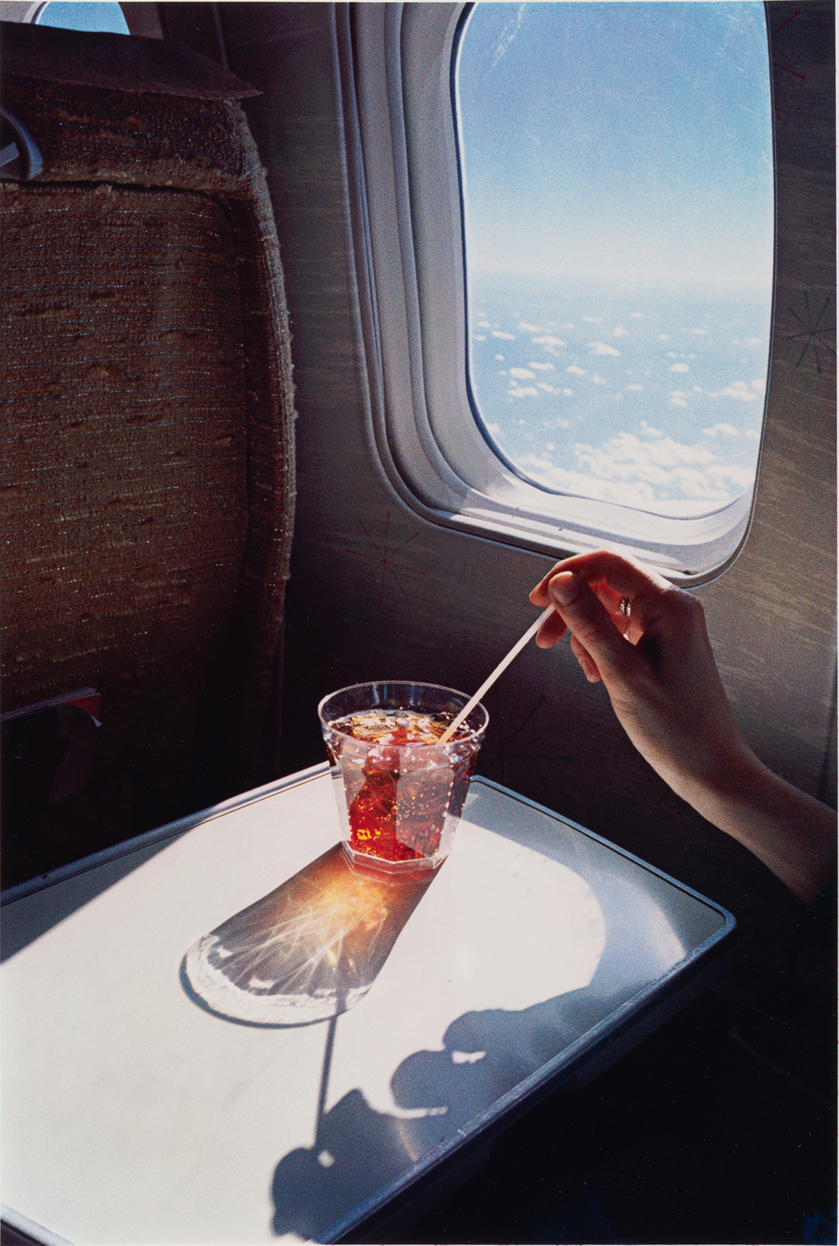 Hand stirring a glass on an aeroplane by photographer William Eggleston