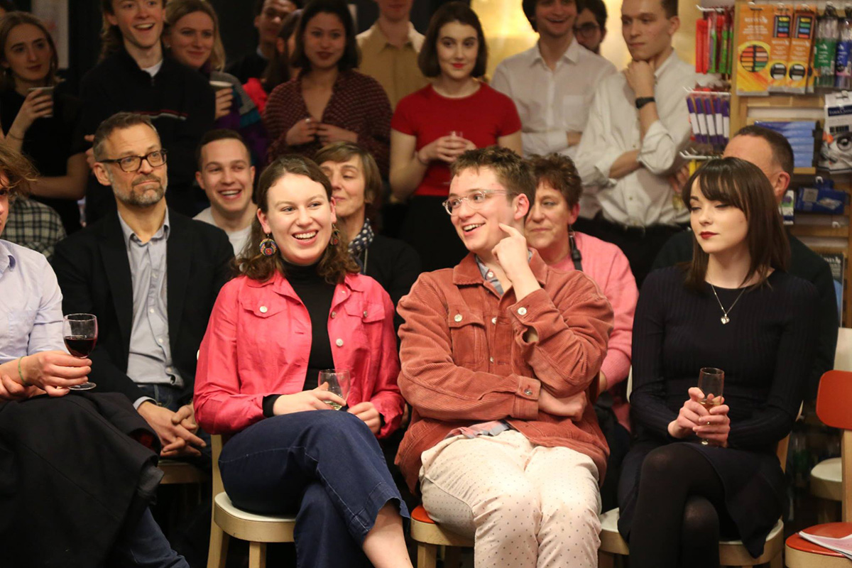 Laughing audience seating and standing in book shop interiors