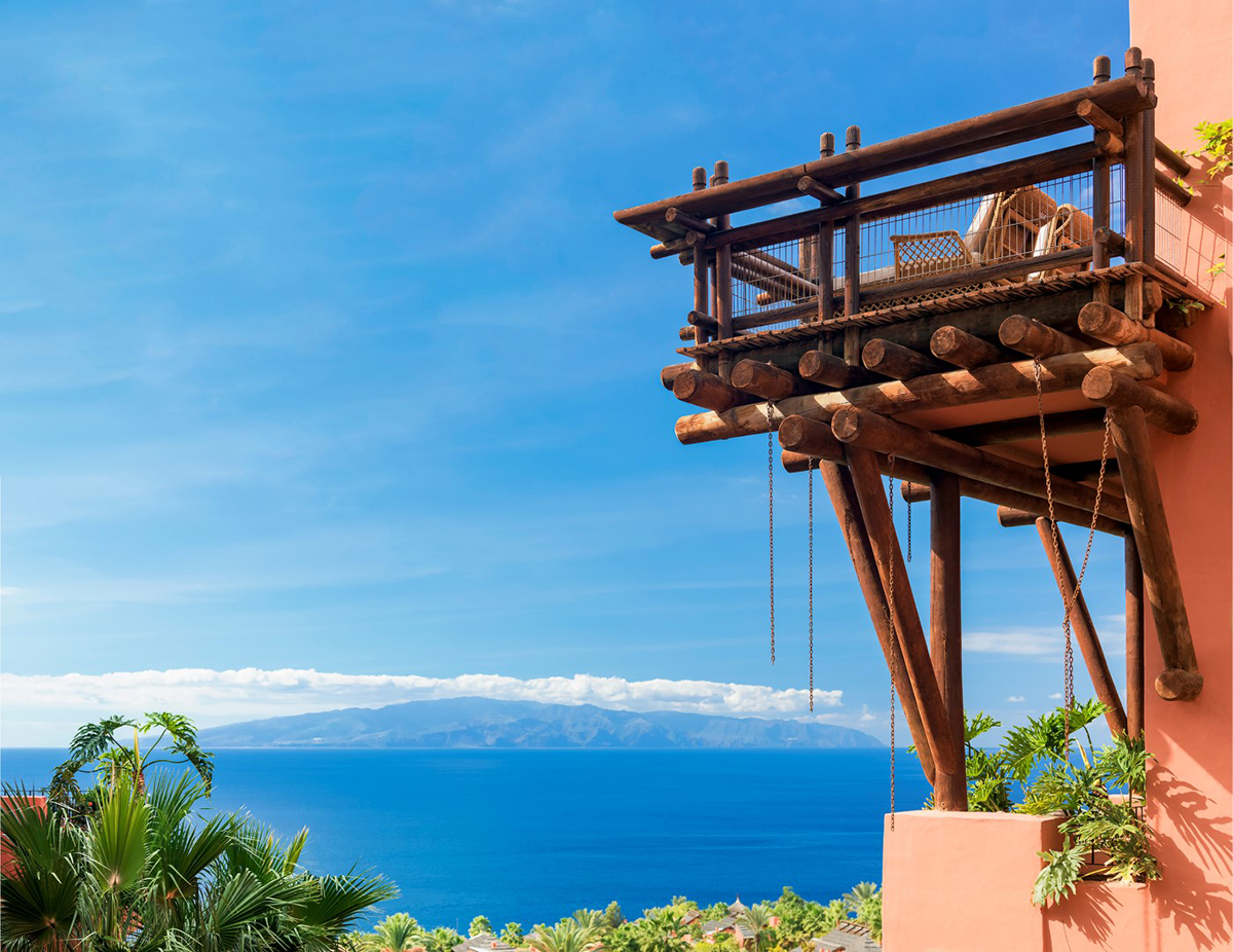 Wooden balcony overhanging a lush green mountainside with the ocean in the distance