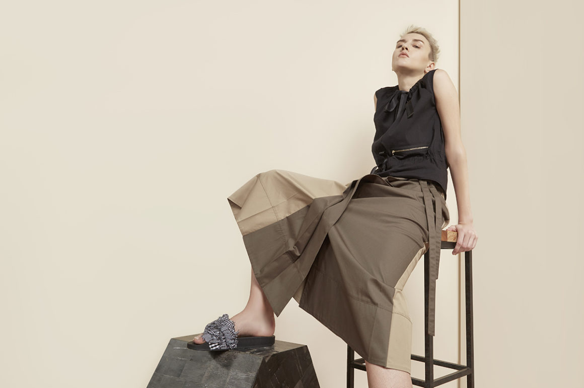 Fashion model poses in skirt and shirt leaning back on a high stool