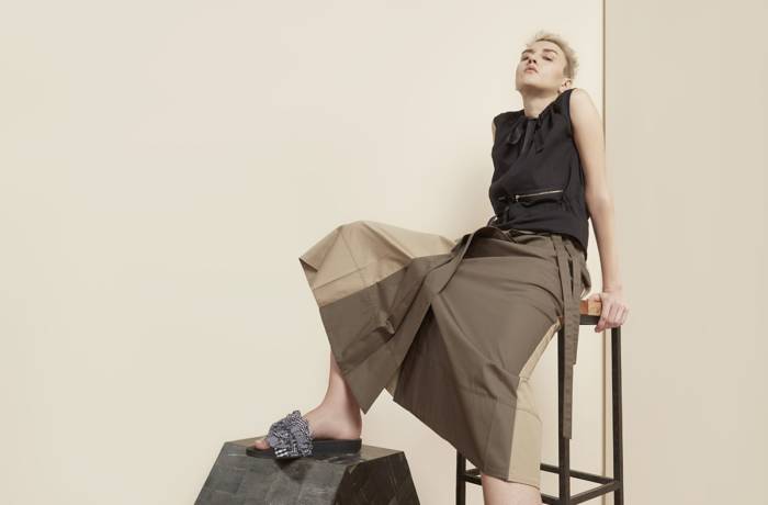 Fashion model poses in skirt and shirt leaning back on a high stool