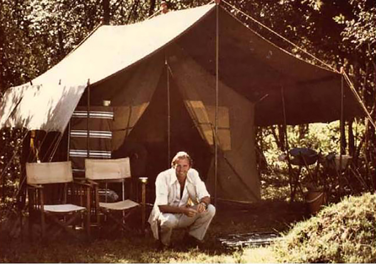 Abercrombie and Kent founder Geoffrey Kent poses crouching in front of luxury safari tent in Tanzania