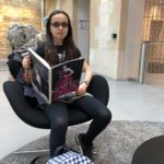 Young girl sits on arm chair reading Alexander McQueen book