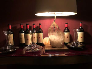 wine bottles lined up against a burgundy wall with a decanter