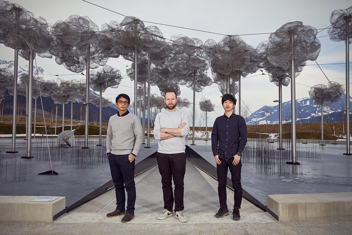 three men standing in front of artistic installation of wire metal trees