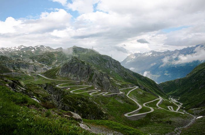 a thin road winding up a lush green mountain with a cloudy sky