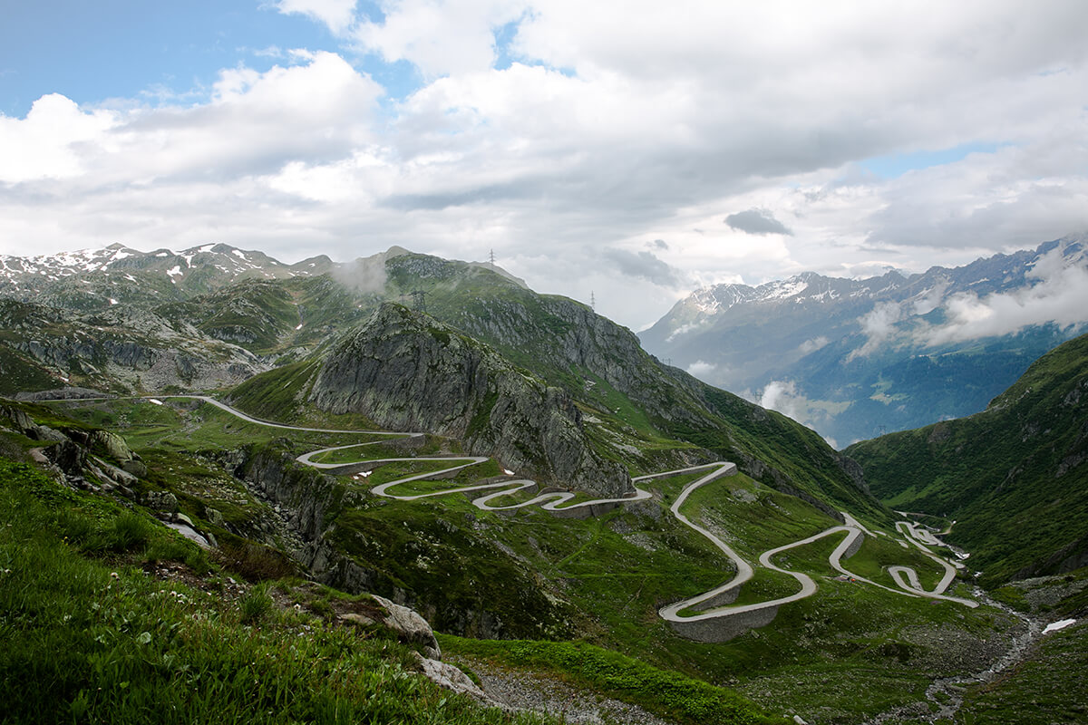 a thin road winding up a lush green mountain with a cloudy sky