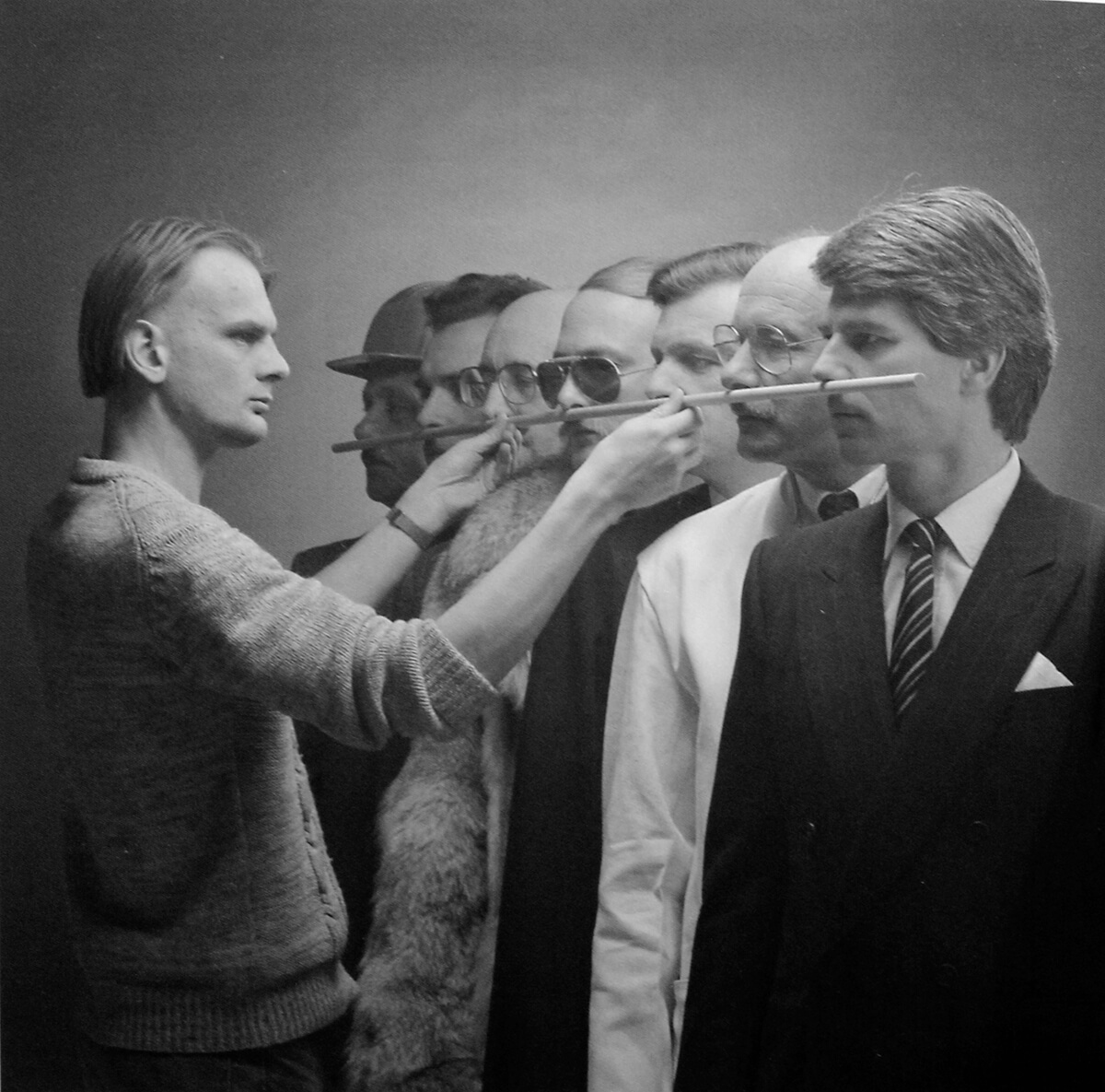 black and white photograph of man holding wooden pole along a line of men's upper lips