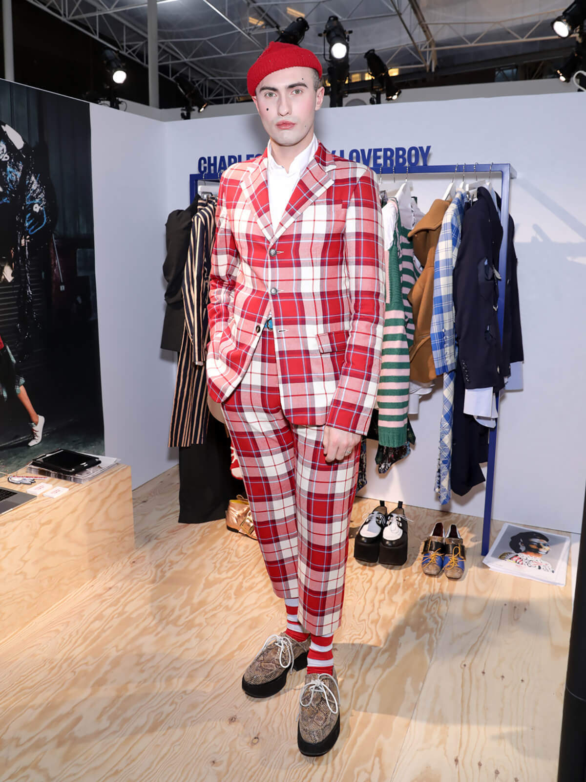 Menswear designer Charles Jeffrey pictured in red chequered suit in front of rail of clothing