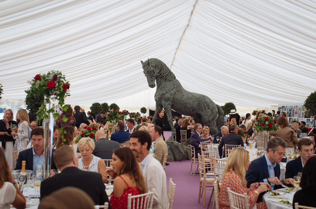 luxury hospitality tent with tables of guests and large sculpture of a horse at the centre 