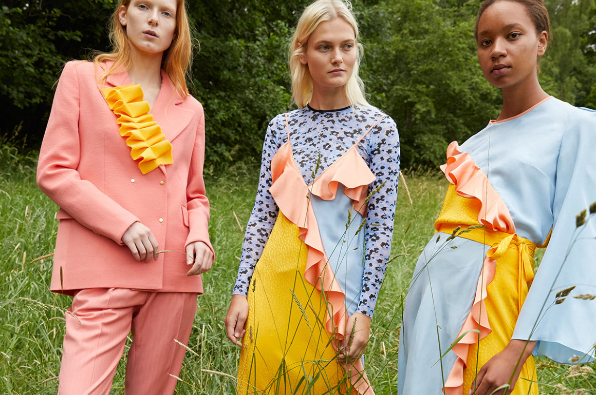 Three female models standing in a field wearing pastel coloured outfits