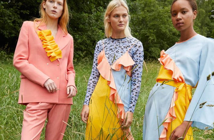 Three female models standing in a field wearing pastel coloured outfits