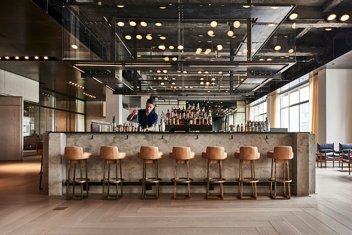 Stylish industrial style bar with leather stools, exposed ceiling and bar tended preparing drinks