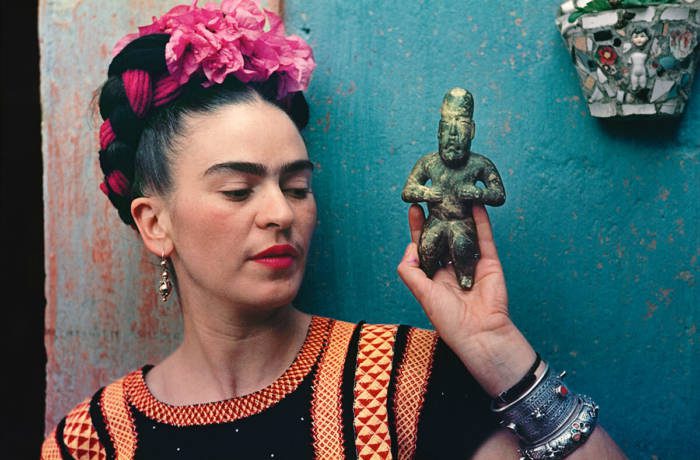 Colour photograph of Mexican artist Frida Kahlo holding a traditional figurine against a blue door