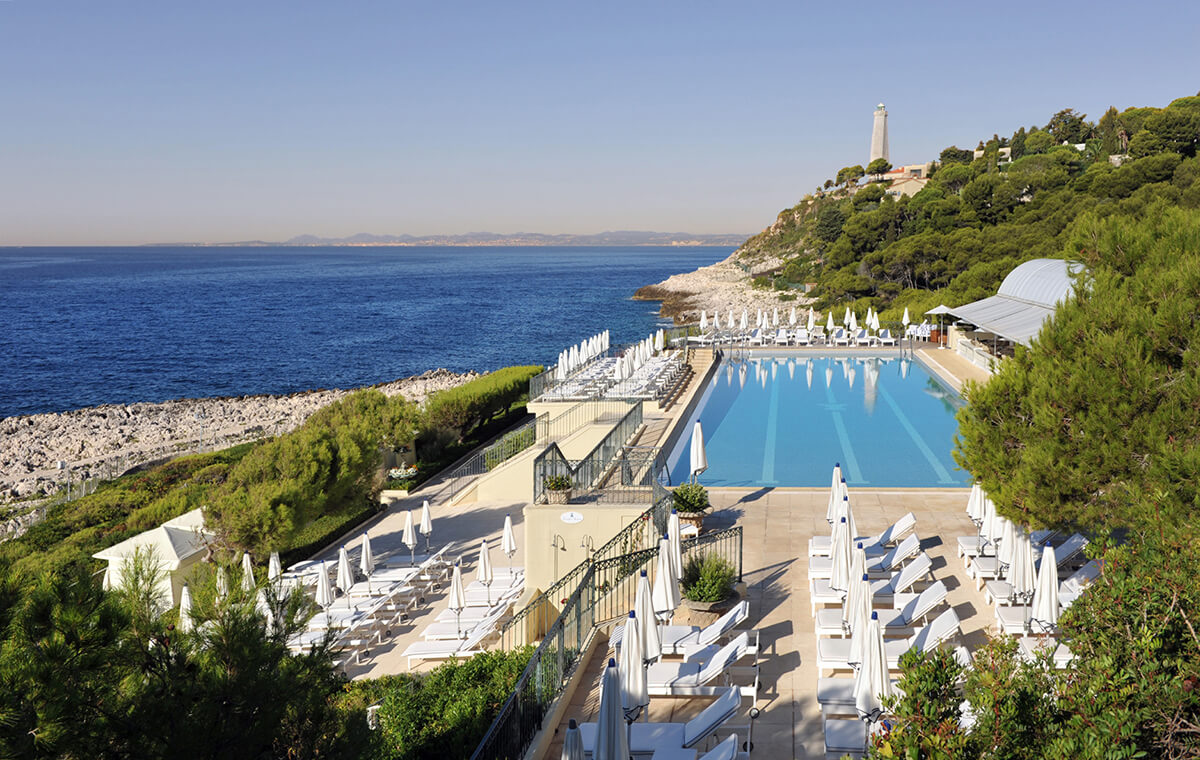 Luxury swimming pool area with large swimming pool surrounded by white umbrellas and sunbeds