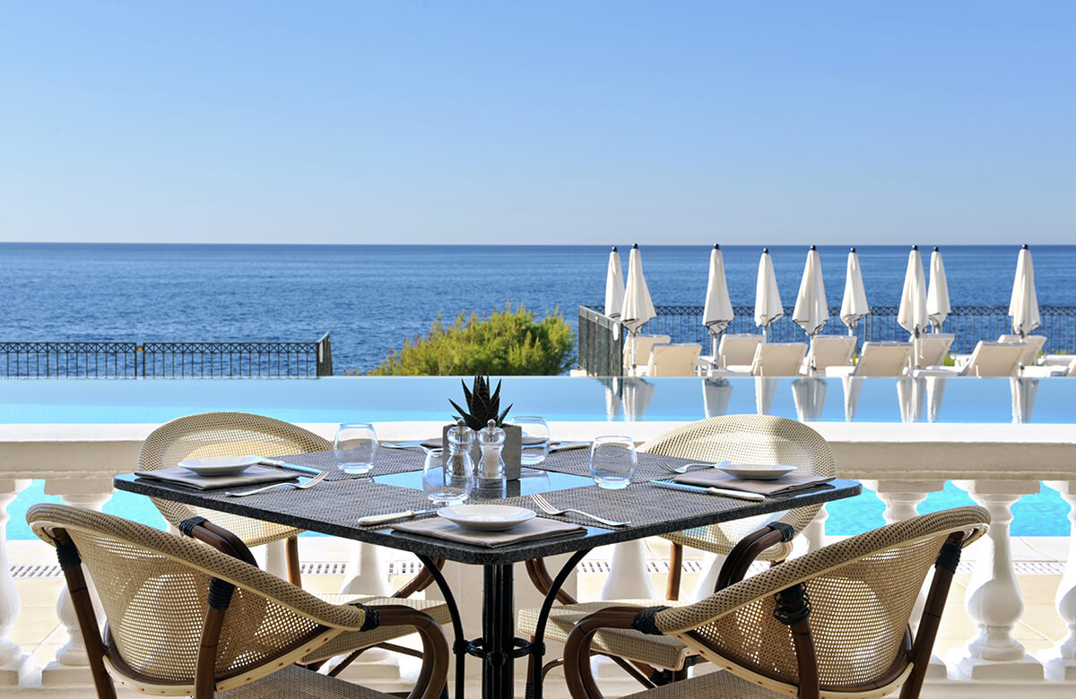 dining table in front of infinity pool with white sun umbrellas and the ocean in the distance