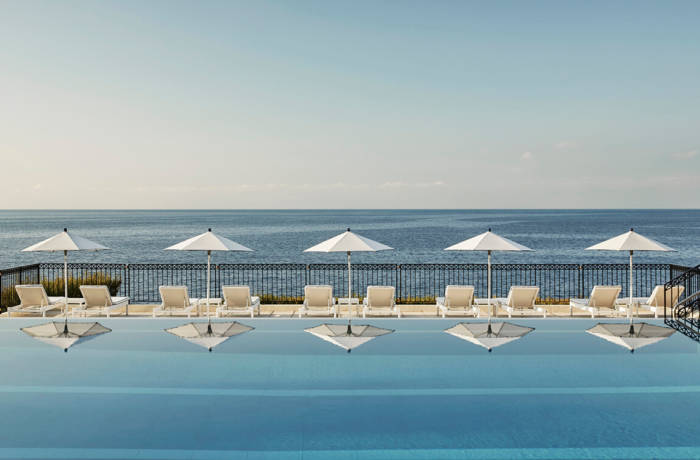 Close up image of swimming pool with white sun umbrellas reflected in the water and the ocean in the distance