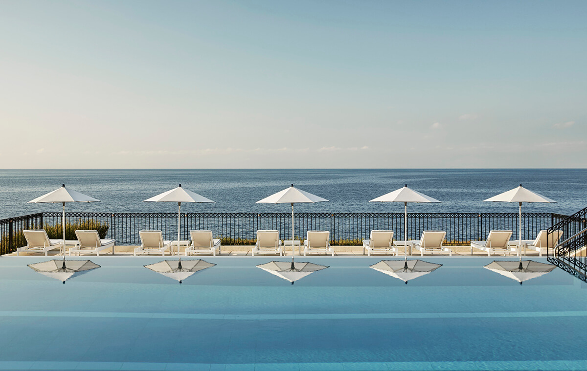 Close up image of swimming pool with white sun umbrellas reflected in the water and the ocean in the distance