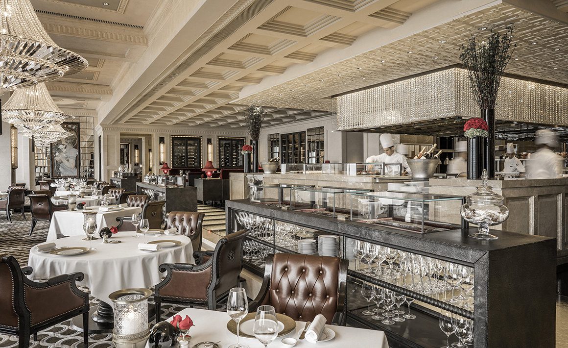 Grand restaurant interiors with plush leather arm chairs, white table cloths and open kitchen