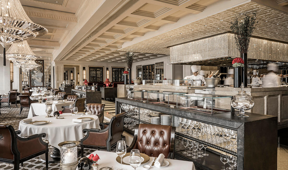 Grand restaurant interiors with plush leather arm chairs, white table cloths and open kitchen