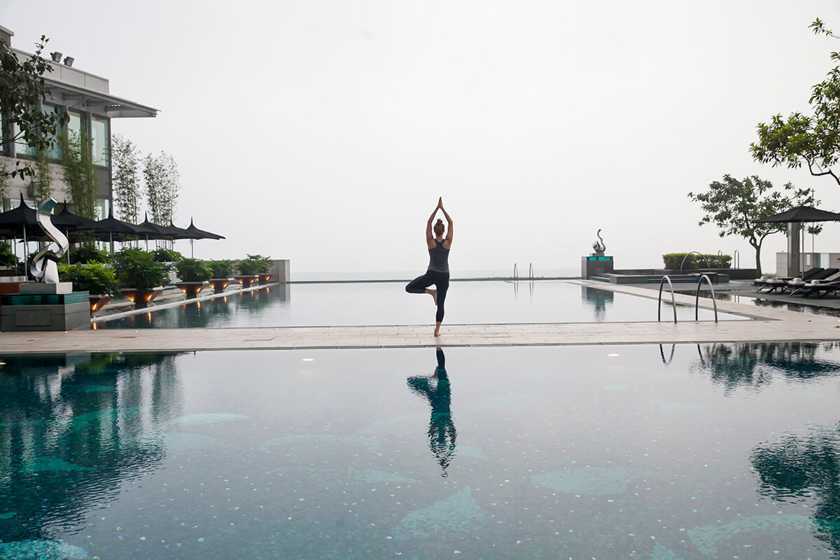 luxury infinity swimming pool with woman practising yoga treepose on centre walkway