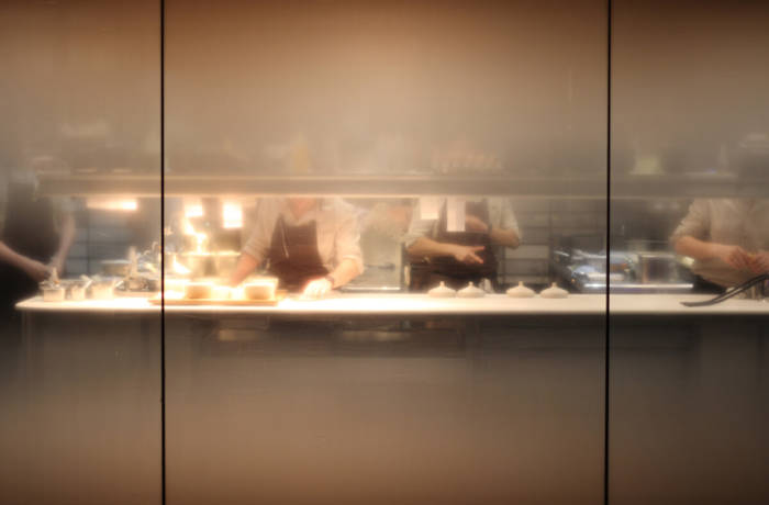 Open restaurant kitchen with window showing chefs preparing food