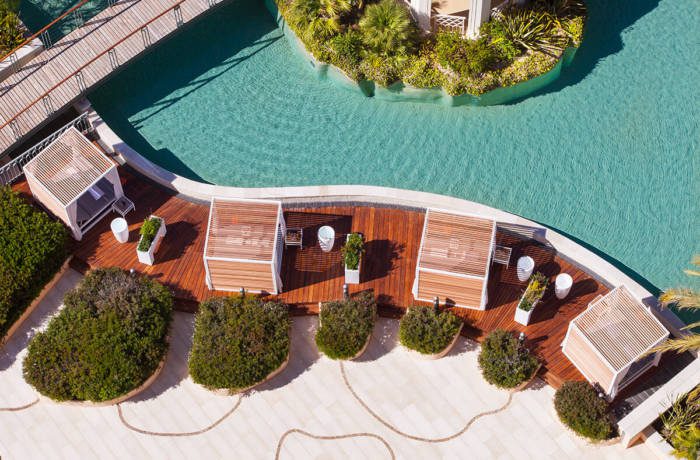 Aerial shot of luxury swimming pool surrounded by wooden decking and cabanas