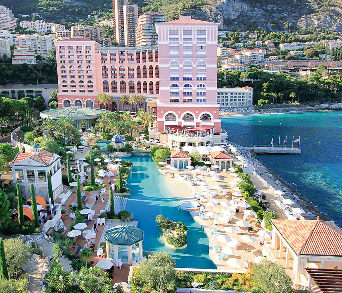 Exterior shot of Monte-Carlo bay hotel with pink mansion house, luxury swimming pool and azure ocean