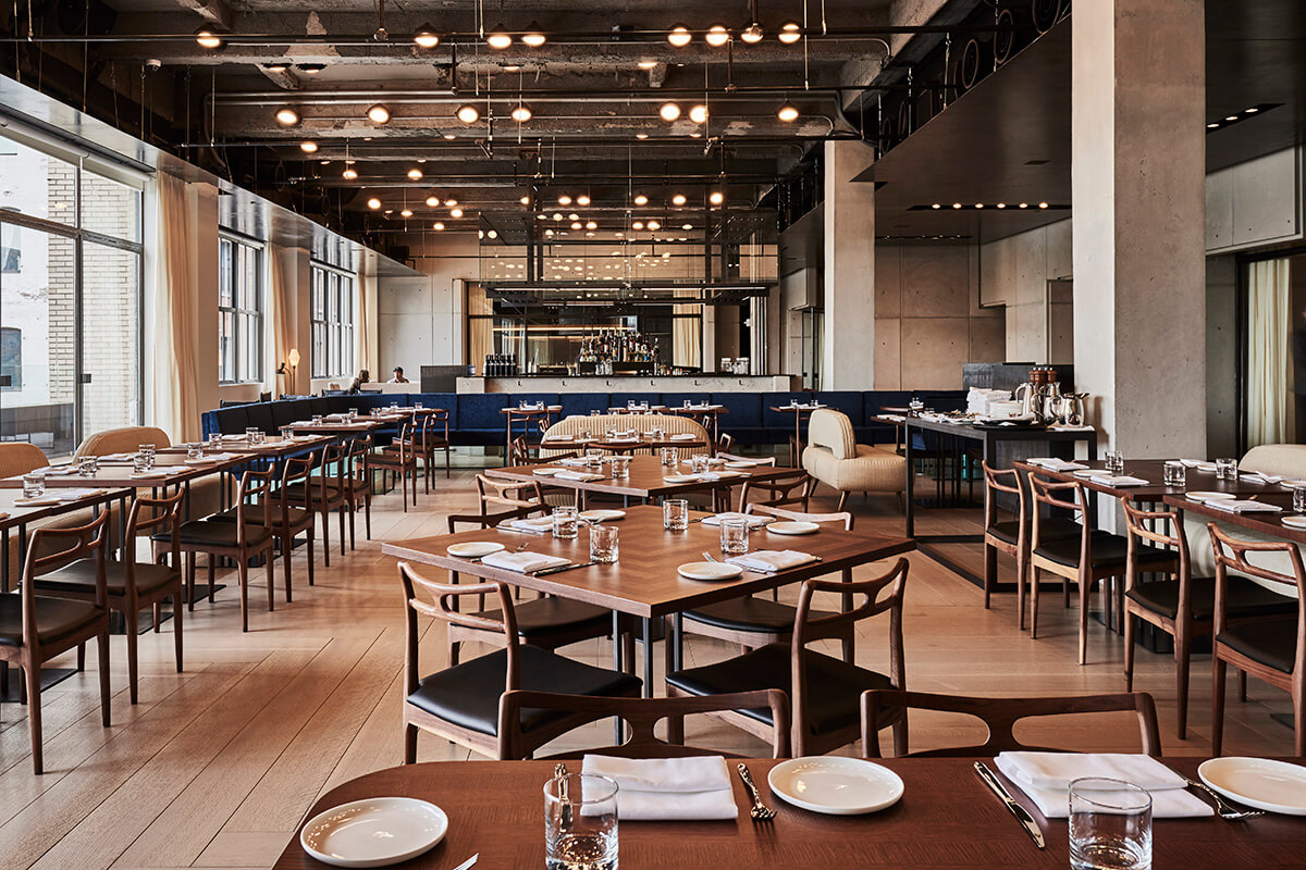 Open plan industrial style dining room with exposed ceiling and square wooden tables