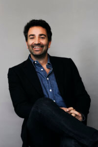 Colour portrait of founder of Spring Studios Francesco Costa wearing a black blazer and a blue shirt, smiling