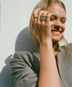 colour headshot of blond girl laughing with hand against face wearing multiple rings