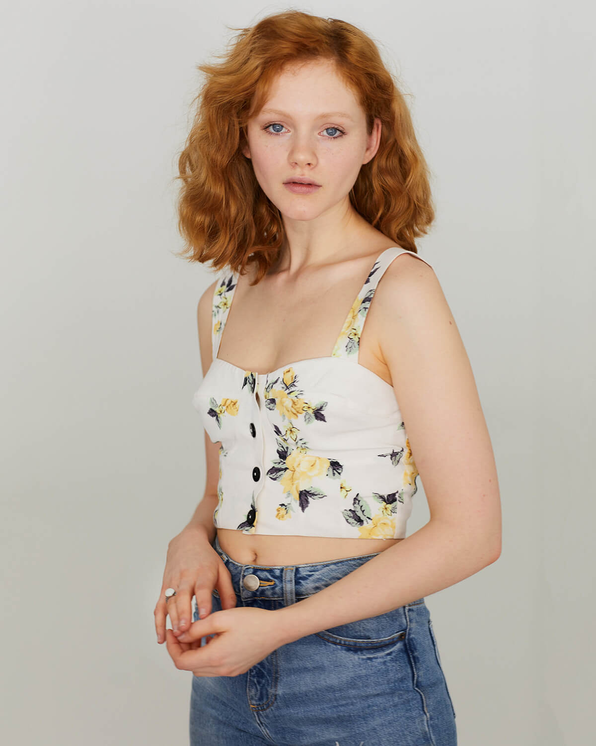 Image of red-haired model standing in jeans and crop top in front of plain background
