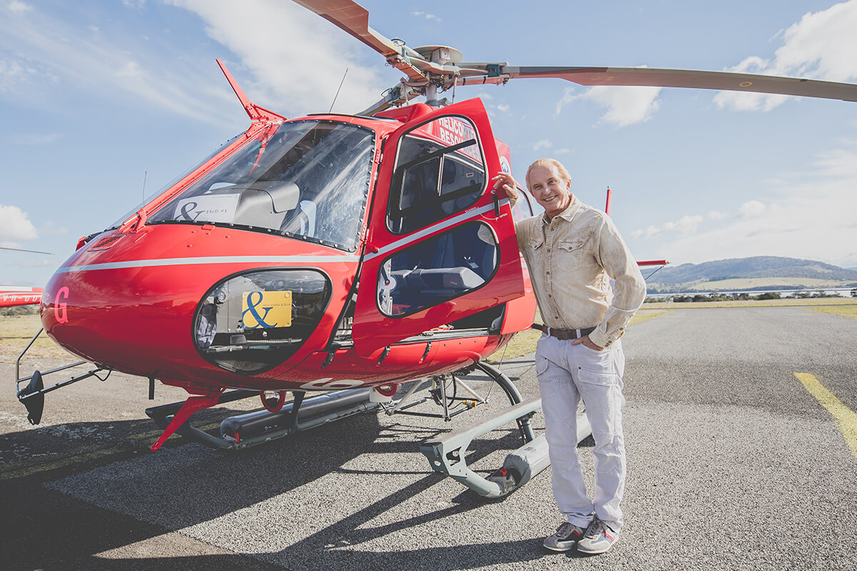 Abercrombie & Kent founder Geoffrey Kent standing next to a red helicopter