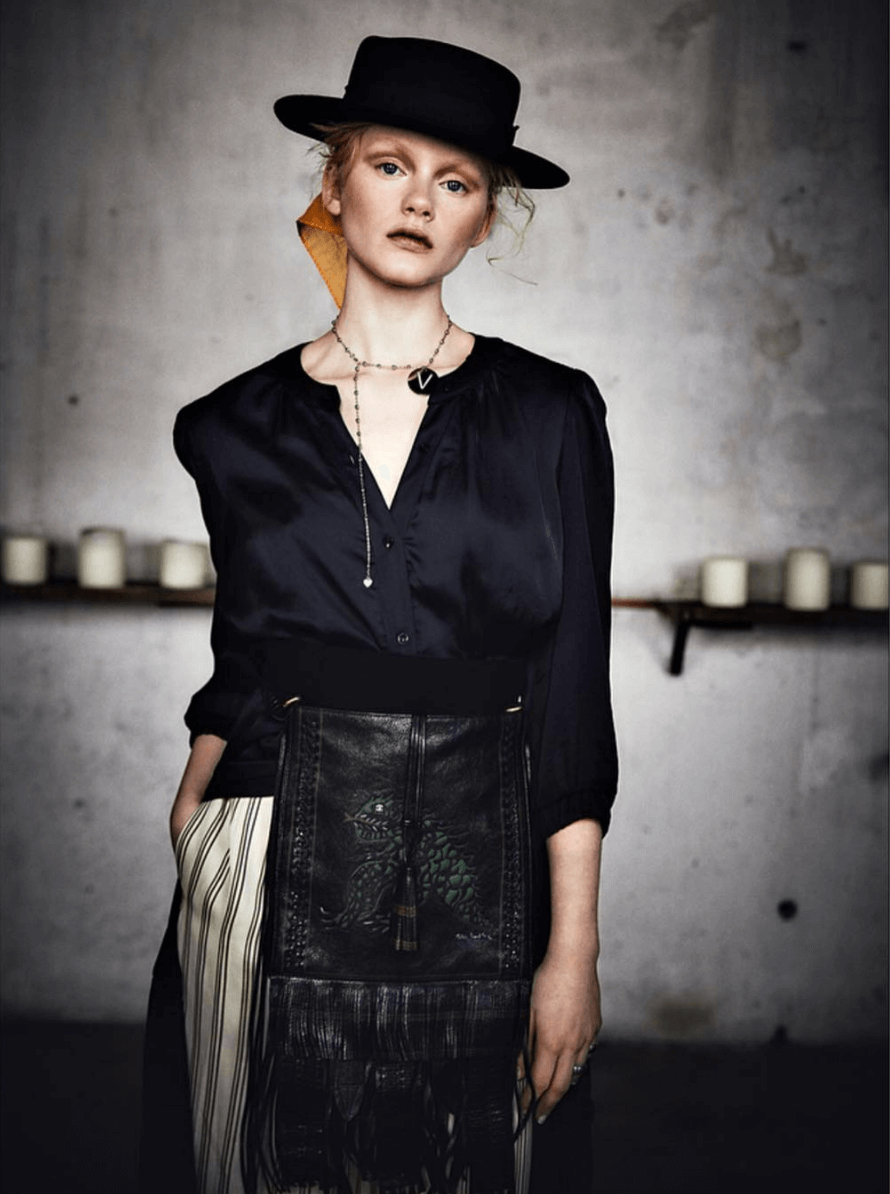 Model on catwalk wearing gothic style outfit black silk shirt, skirt and hat