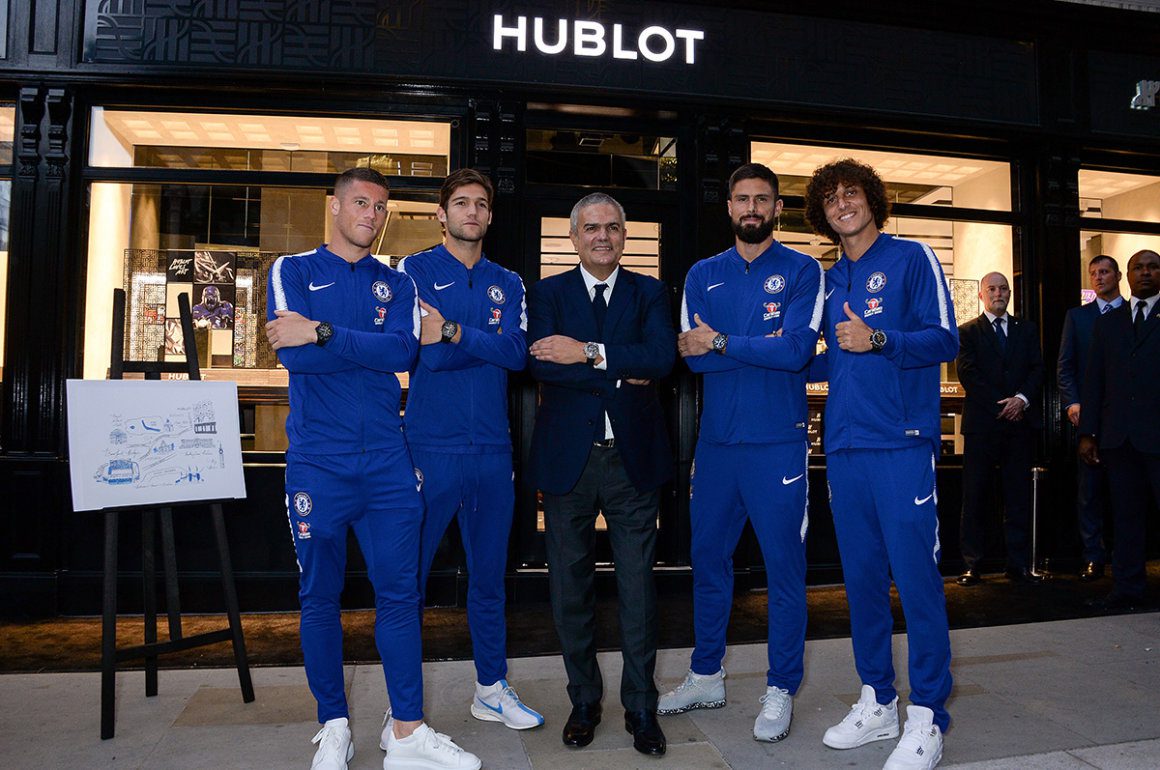 Chelsea FC football players in their blue tracksuits standing outside of a Hublot shop front with Ricardo Guadalupe