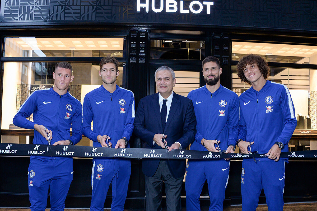 Chelsea FC football players in their blue tracksuits cutting a Hublot ribbon outside the Hublot shop front with Ricardo Guadalupe