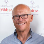 Portrait of british entrepreneur John Caudwell in front of Caudwell Children sign