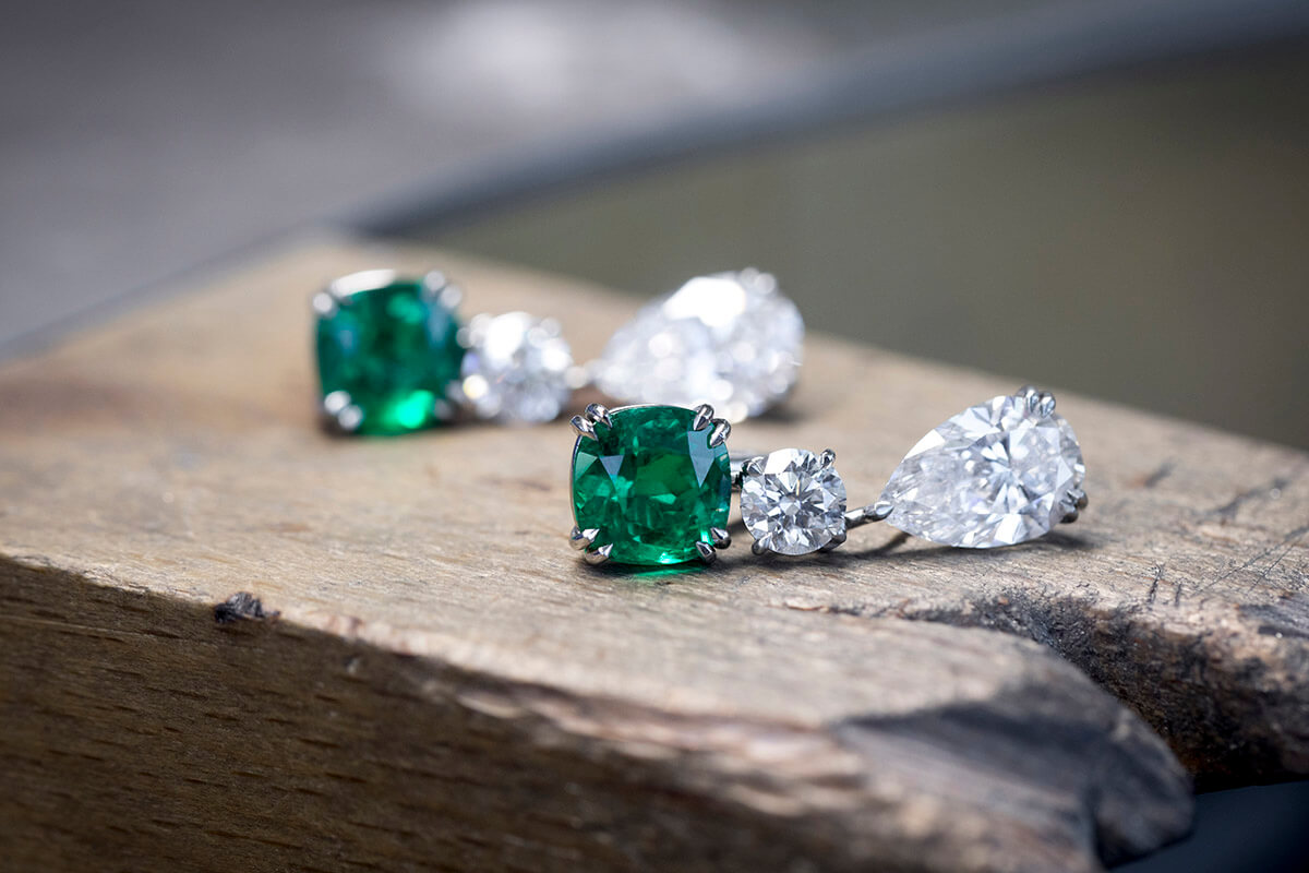 Emerald and diamond earrings laid on a wooden slate