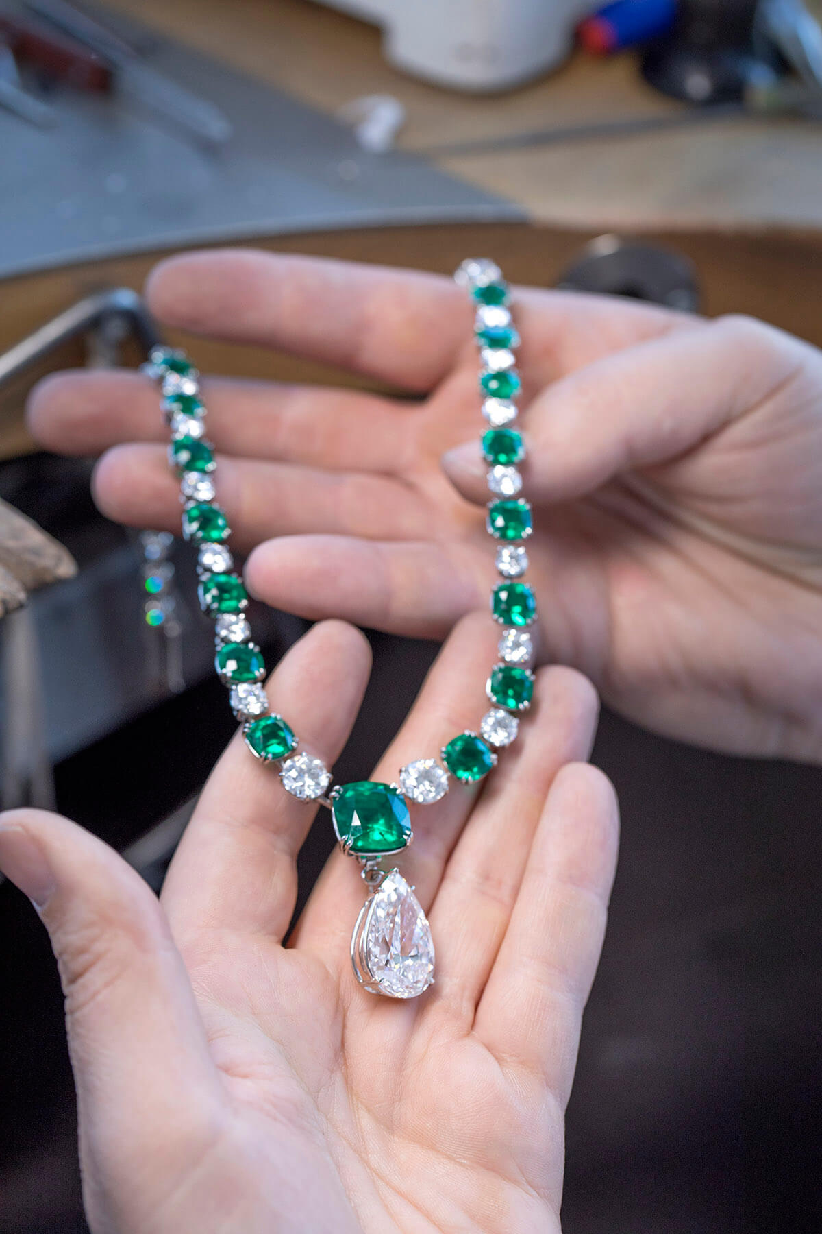 An emerald and diamond necklace draped across hands 