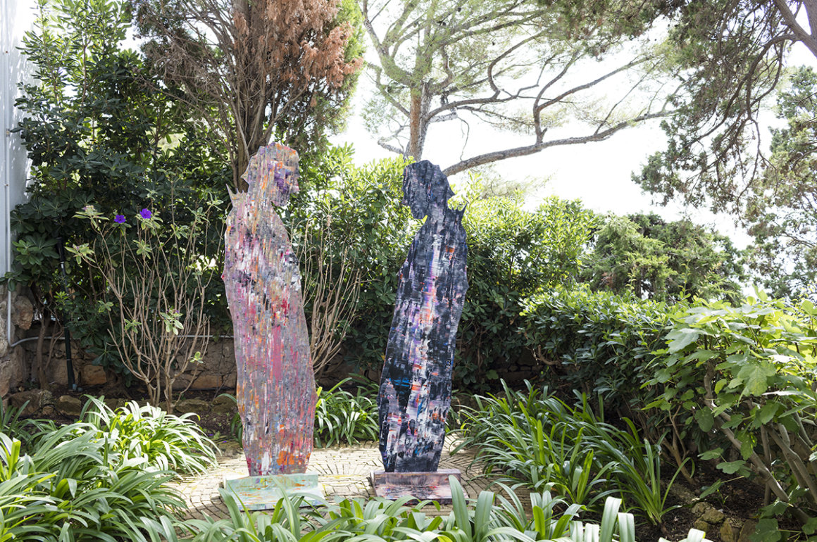 Two colourful sculptures of men standing in a lush green garden