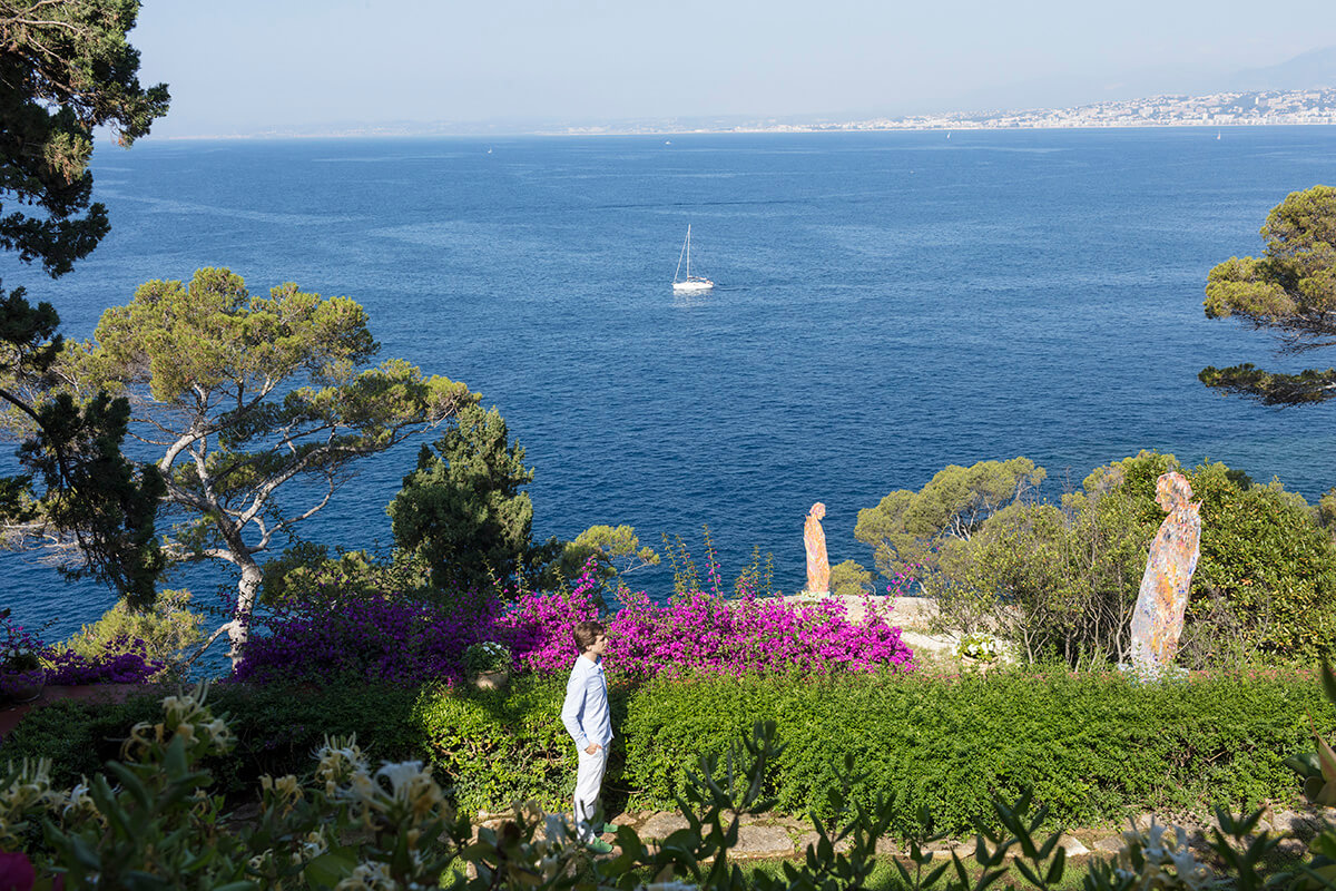 Artist Sassan Behnam-Bakhtiar standing in garden with his sculptures and the ocean in the distance