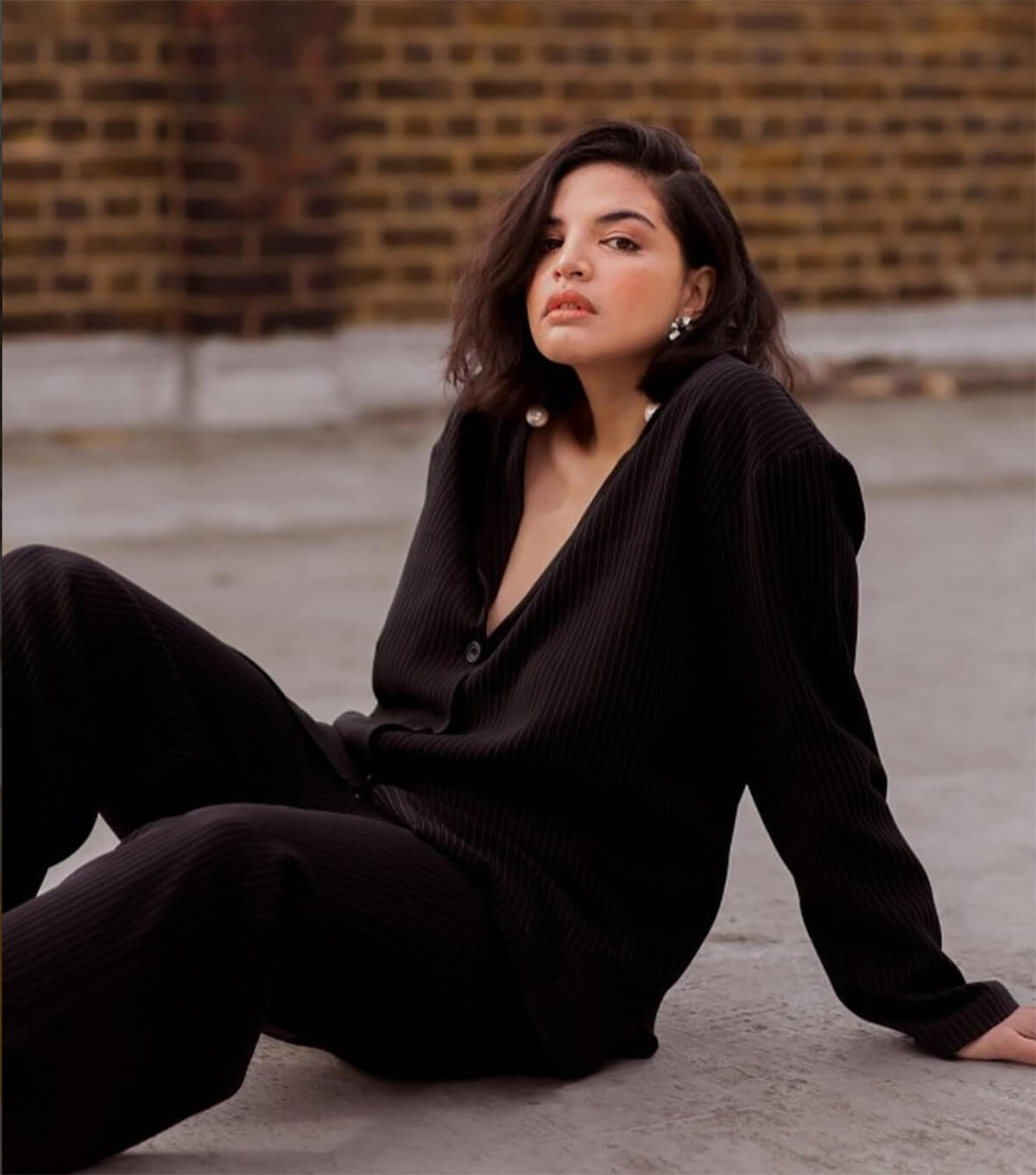 Model wearing black jumpsuit reclining on the ground