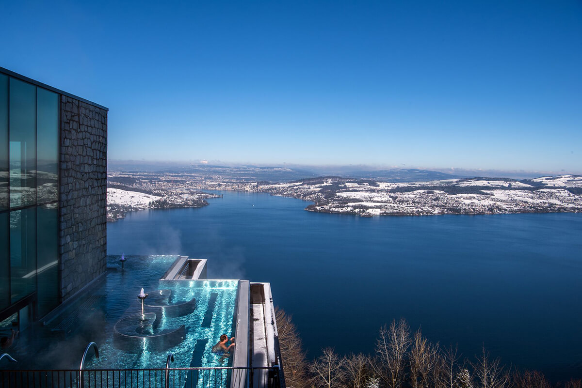 Stunning outdoor infinity pool overhanging a lake with snowing landscapes in the distance