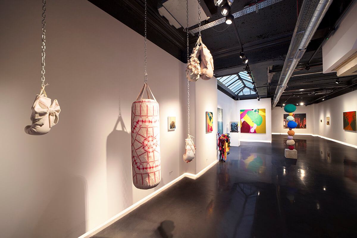 gallery view of art exhibition with hanging punch bag and colourful paintings on the walls