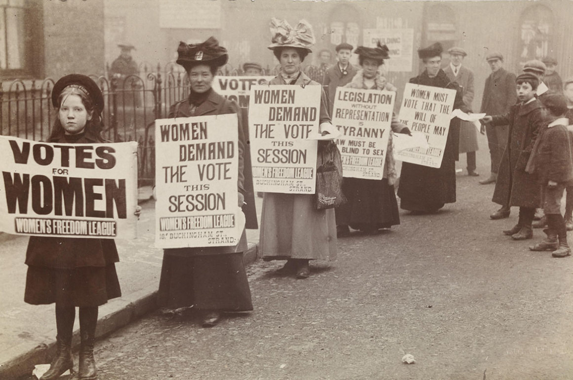 Historical suffragette photograph in black and white of women's parade holding signs with the suffrage message