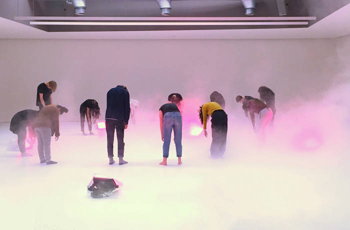 Performance art scene of people hanging over surrounded by mist and pink lights